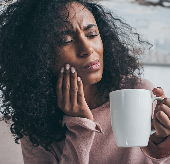 Pained woman holding coffee cup needs Houston emergency dentist