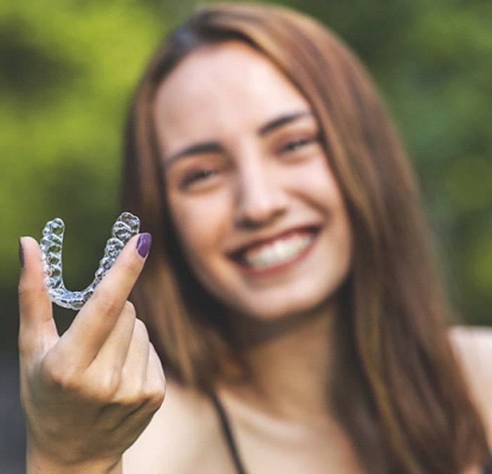 Woman smiling while holding up Invisalign in Houston