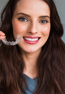 woman smiling while holding Invisalign aligners