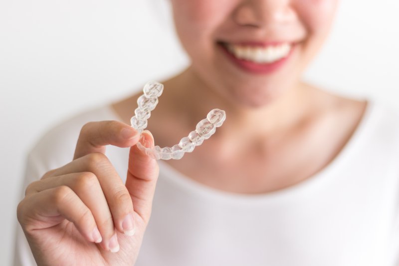 Woman smiling while holding Invisalign retainer