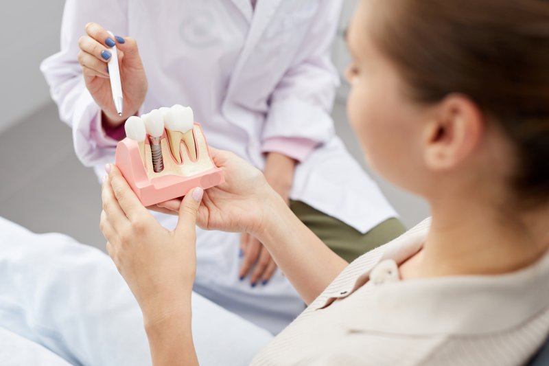A dentist pointing to a model dental implant held by a patient